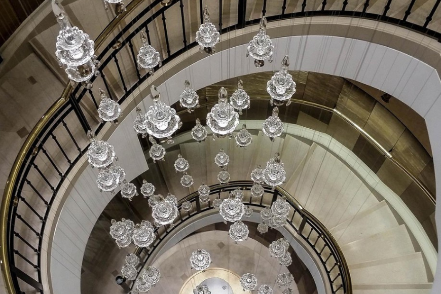 מבט על גרם מדרגות ספירלי מפואר עם מעקה ברזל שחור ואשכול נברשות קריסטל תלויים במרכז החלל.